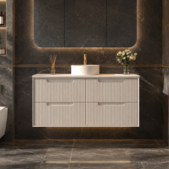 A modern bathroom vanity setup with a white floating sink cabinet, a white vessel sink, a large backlit rectangular mirror, and a gold faucet, set against dark marble walls and floor. A white toilet is visible to the left, and a glass shower enclosure appears on the right.